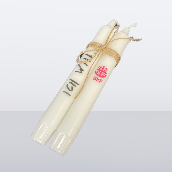 Zwei weiße Stabkerzen mit Juteband gebunden, eine mit „ICH WILL“ beschriftet, die andere mit SkF-Logo
