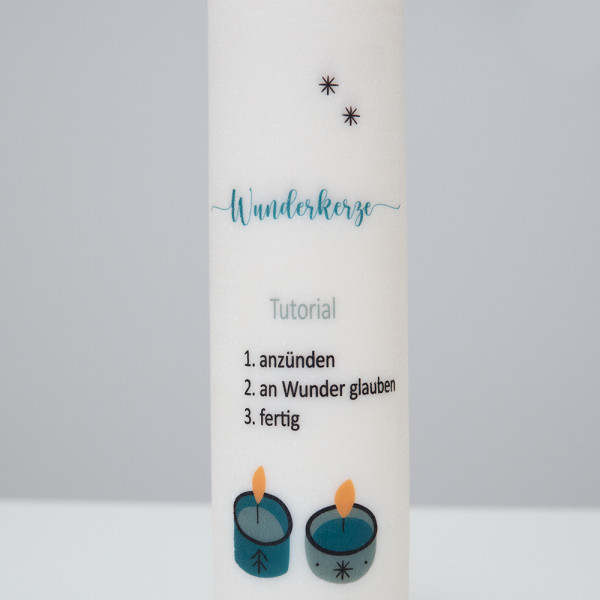 Nahaufnahme einer weißen Kerze mit dem Schriftzug „Wunderkerze“, verziert mit kleinen Sternen und zwei brennenden Teelichtern