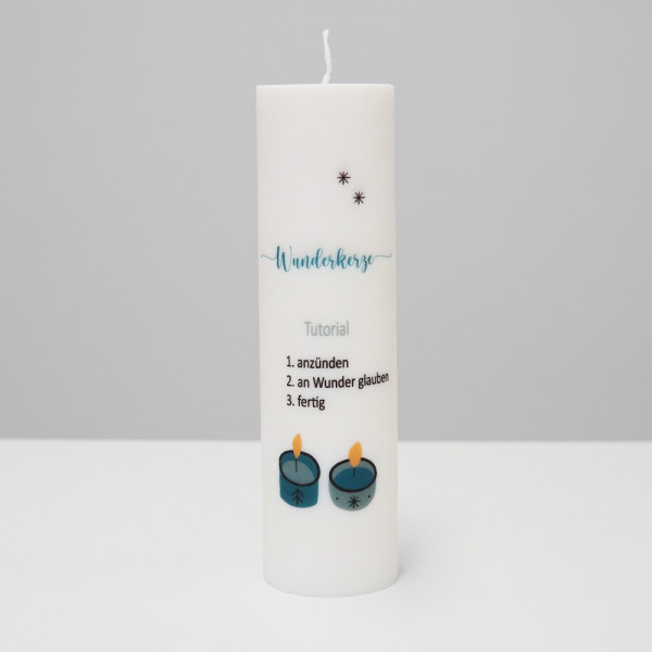 Weiße Kerze mit der Aufschrift „Wunderkerze“, verziert mit kleinen Sternen und zwei brennenden Teelichtern