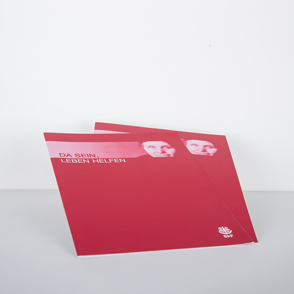Zwei rote Einlegemappen mit der Aufschrift „Da sein leben helfen" und dem Porträt einer Frau
