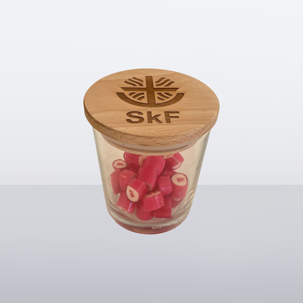 Glas mit Holzdeckel und SkF-Logo, befüllt mit roten Bonbons